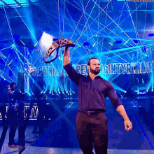 a man in a blue shirt holds up a wrestling championship belt in front of a sign that says revolution