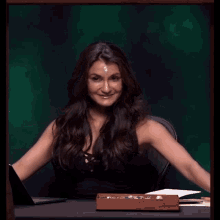 a woman is sitting at a desk with her arms outstretched and a box of jewelry in front of her .