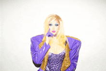 a woman wearing a purple jacket and leopard print dress holds her finger to her mouth