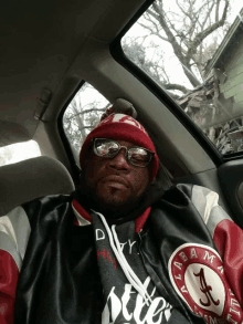 a man in a car wearing a alabama jacket and a red beanie