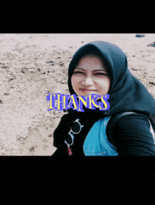 a woman wearing a black head scarf and a blue vest is standing on a beach with the words thanks above her