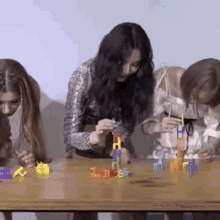 three women are sitting at a table playing with toys and one of them is holding a toy that says t.