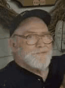 a man with a beard and glasses is wearing a hat and a black shirt .