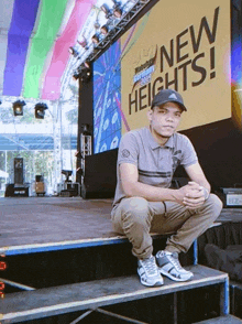 a man sits on the steps of a stage in front of a sign that says new heights