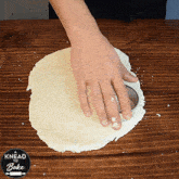 a person is kneading a piece of dough on a wooden table with a sign that says knead to bake