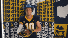 a man wearing a cowboy hat holds a football in front of a wall that says toledo team on it