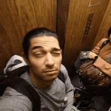 a man in an elevator with his eyes closed and a backpack that says gregory on it