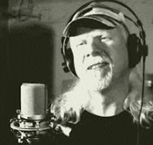 a man wearing headphones and a hat is standing in front of a microphone in a black and white photo .