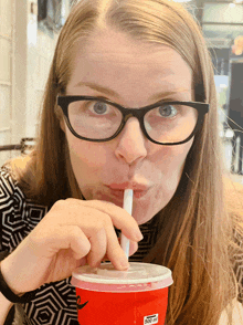 a woman wearing glasses drinks through a straw from a red cup that says 500 ml