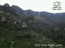 an aerial view of a village in the middle of a mountain with a waterfall coming down the side of the mountain .