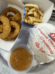 a hamburger with onion rings and french fries sits next to a cup of sauce