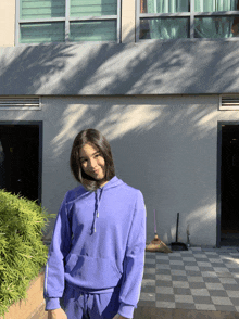 a girl in a purple hoodie is standing in front of a building