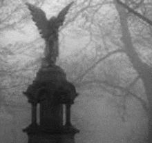 a black and white photo of a statue of an angel in a cemetery in the fog .