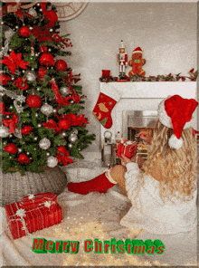 a woman in a santa hat sits in front of a christmas tree with the words merry christmas above her