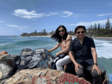 a man and a woman sit on a rock near the ocean holding a sign that says anzai