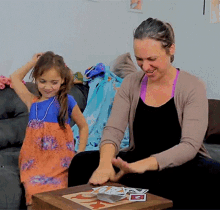 a woman and a little girl are playing a game with cards on a table and one of the cards has the letter e on it