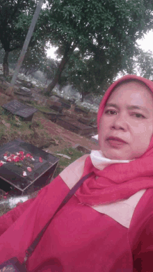 a woman in a red head scarf takes a selfie in front of a cemetery