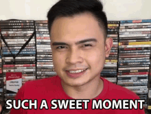 a man in a red shirt is smiling in front of a stack of dvds and the words such a sweet moment .