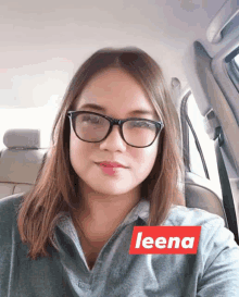 a woman wearing glasses is sitting in a car with a red sticker that says leena on it