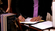 a man in a purple tie is writing on a piece of paper in front of a book titled crimes & angels