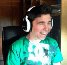 a young man wearing headphones and a green shirt is sitting in a chair and smiling .