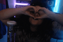 a person making a heart shape with their hands in front of a happy halloween sign