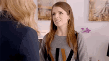 a woman in a grey sweater is smiling while talking to another woman .