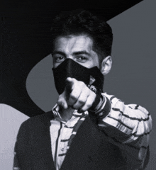 a man wearing a black face mask points at the camera