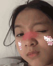 a girl with hello kitty stickers on her face looks at the camera