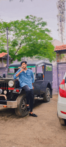 a man in a blue shirt leans against a black jeep with a license plate that says ' tc ' on it