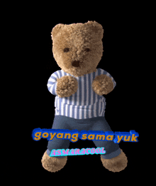 a teddy bear wearing a blue and white striped shirt is holding a sign that says goyang sama yuk