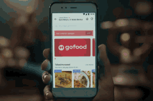 a person is holding a smart phone with a gofood app open