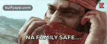 a man wearing a bandana on his face is talking on a cell phone and saying `` na family safe '' .