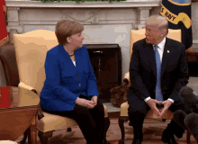 a man in a suit and tie sits next to a woman in a blue jacket in front of a us navy flag