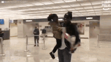 a man is carrying a little girl in his arms in an airport with a sign that says men behind him