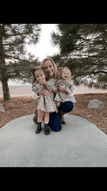 a woman kneeling down holding two little girls