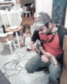 a man is kneeling down playing a guitar while a little girl plays drums in the background