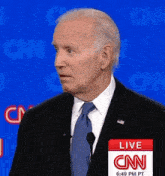 a man in a suit and tie stands in front of a microphone with a live cnn sign behind him