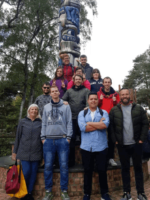 a group of people posing in front of a totem pole one of the men is wearing a sweatshirt that says california steelies