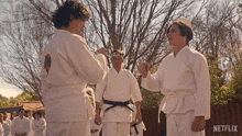 a group of men in white karate uniforms are standing in front of a fence with a netflix logo on it