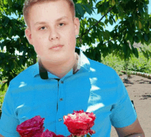 a young man in a blue shirt holds two red roses in his hand