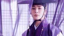 a man wearing a purple hat and a purple robe stands in front of a purple curtain ..