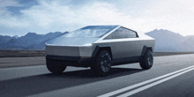 a tesla cybertruck is driving down a highway with mountains in the background