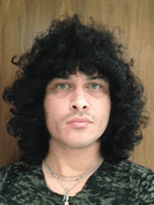 a man with curly hair is wearing a necklace and a camouflage shirt