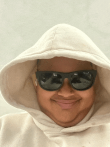 a person wearing sunglasses and a white hoodie smiles for the camera