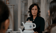 a woman is sitting at a table with a teapot on it