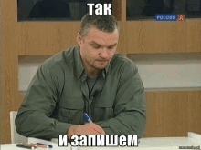 a man sitting at a desk with a pen in his hand with a meme written in russian