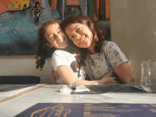 two girls sit at a table in front of a painting that says ' a ' on it