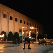 a man is kneeling down in front of a building that is lit up at night