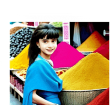 a little girl in a blue dress is standing in front of a pile of colored powders